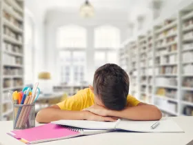 Chłopiec z głową na biurku pełnym zeszytów