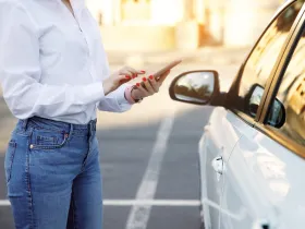 Kobieta trzymająca smartfon stojąc obok samochodu