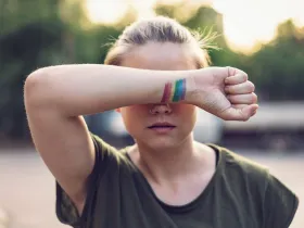 Kobieta zakrywająca oczy ręką z namalowaną tęczową flagą