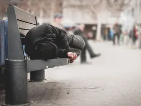 Osoba w kryzysie bezdomności leżąca na ławce