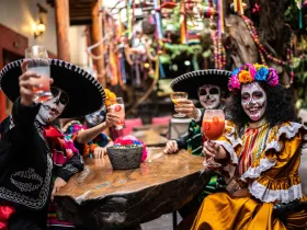 Osoby w strojach Día de Muertos wznoszą toasty przy stole