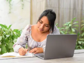 Latynoska kobieta przy laptopie pisze w notatniku