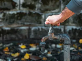 Ręka osoby próbuje odkręcić stary, zardzewiały kran na zewnątrz