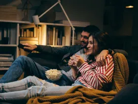 Miło spędzająca czas para ogląda film w domu, trzymając miskę popcornu