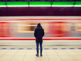 Osoba samotnie stoi na peronie metra, patrząc na przejeżdżający pociąg