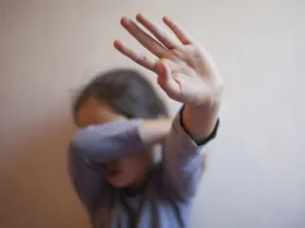 Dziecko zakrywa twarz ramieniem i dłonią w geście obronnym, wycofania lub strachu
