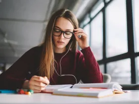 Skoncentrowana studentka w okularach i słuchawkach uczy się w jasnym wnętrzu