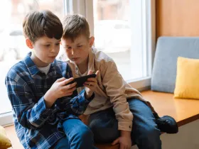  Dwóch chłopców siedzi przy oknie, wspólnie oglądając coś na smartfonie