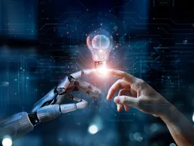 Robotyczna i ludzka dłoń dotykają się przy żarówce – symbol innowacji i AI