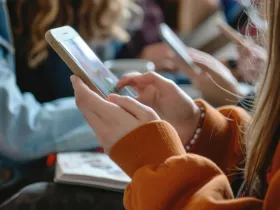 Bliska perspektywa rąk osoby korzystającej ze smartfona. W tle widać innych ludzi
