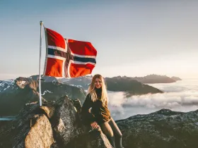 Blondwłosa dziewczyna w górach, pozująca z flagą Norwegii