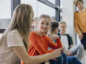 Grupa nastolatków rozmawia i patrzy na telefon w jasnym pomieszczeniu