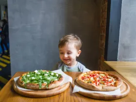 Dziecko siedzi w restauracje, przed nim stoją dwie pizze