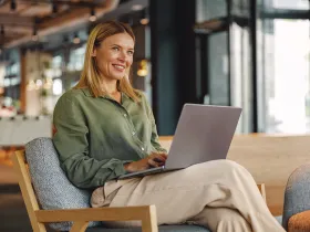 Uśmiechnięta kobieta w biurze pracuje na laptopie, siedząc zrelaksowana w fotelu