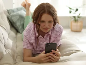 Dziewczyna w kratkowanej koszuli leży na kanapie i patrzy na telefon