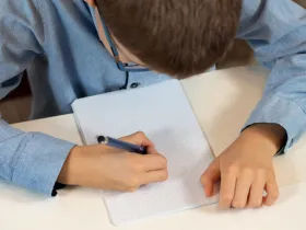 Dziecko pisze w zeszycie – ilustracja do artykułu o czynnikach wpływających na wyniki w nauce