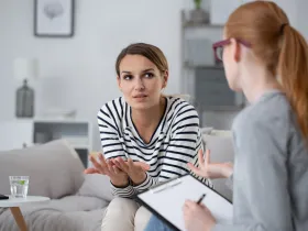 Psychoterapeutka rozmawia z pacjentką w gabinecie, notując przebieg sesji