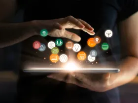Osoba trzyma tablet z ikonami aplikacji unoszącymi się nad nim – symbol AI w marketingu