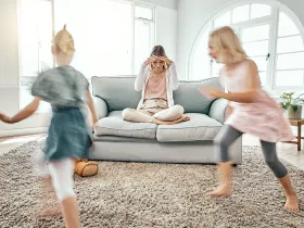 Matka w stresie siedzi na kanapie, podczas gdy dwójka małych dzieci biega w tle