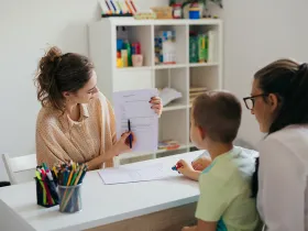 Nauczycielka rozmawia z matką i chłopcem, pokazując na kwestionariusz lub test